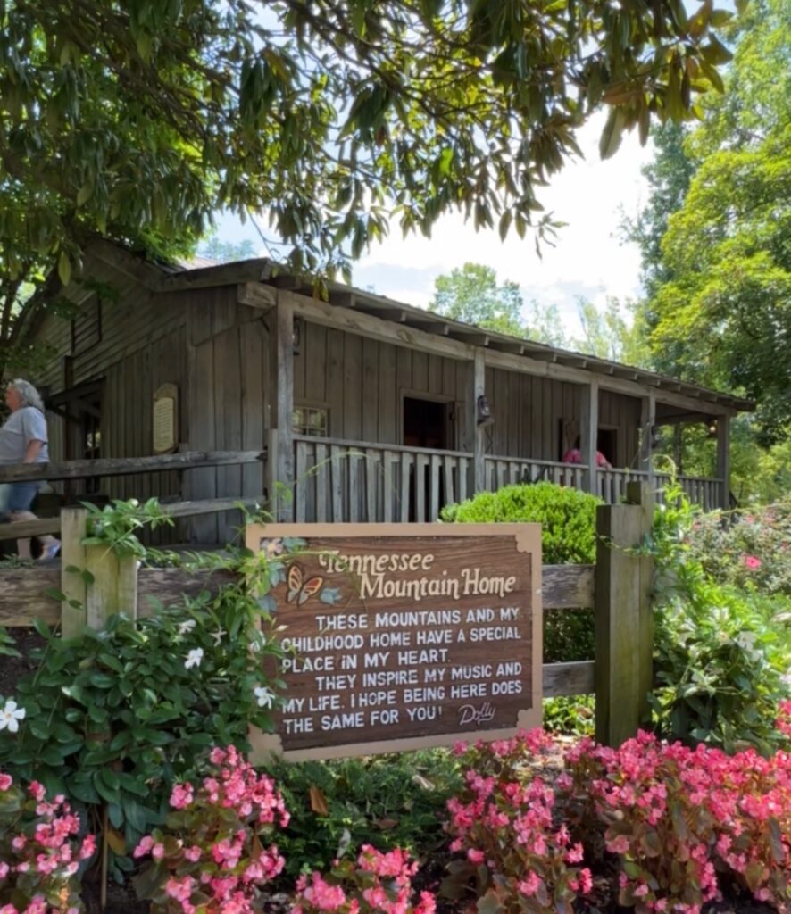 The exterior of Dolly’s Tennessee Mountain Home and dedication plaque surrounded by flowers and trees at Dollywood 